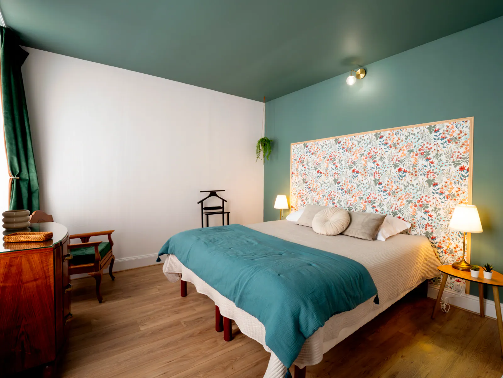 Chambre avec murs bleu-vert, lit double couverture turquoise, tête de lit motifs floraux
