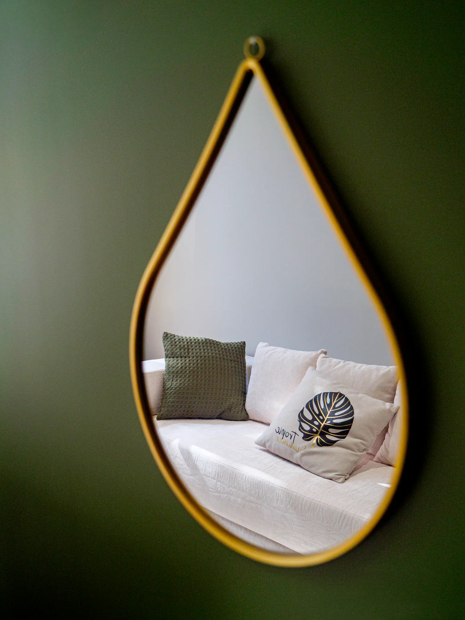 Miroir mural en forme de goutte avec encadrement doré, niche décorée de coussins et linge de maison.