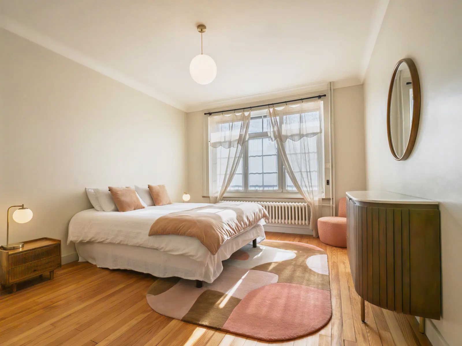Chambre ensoleillée avec lit blanc, mobilier vintage en bois et miroir rond doré