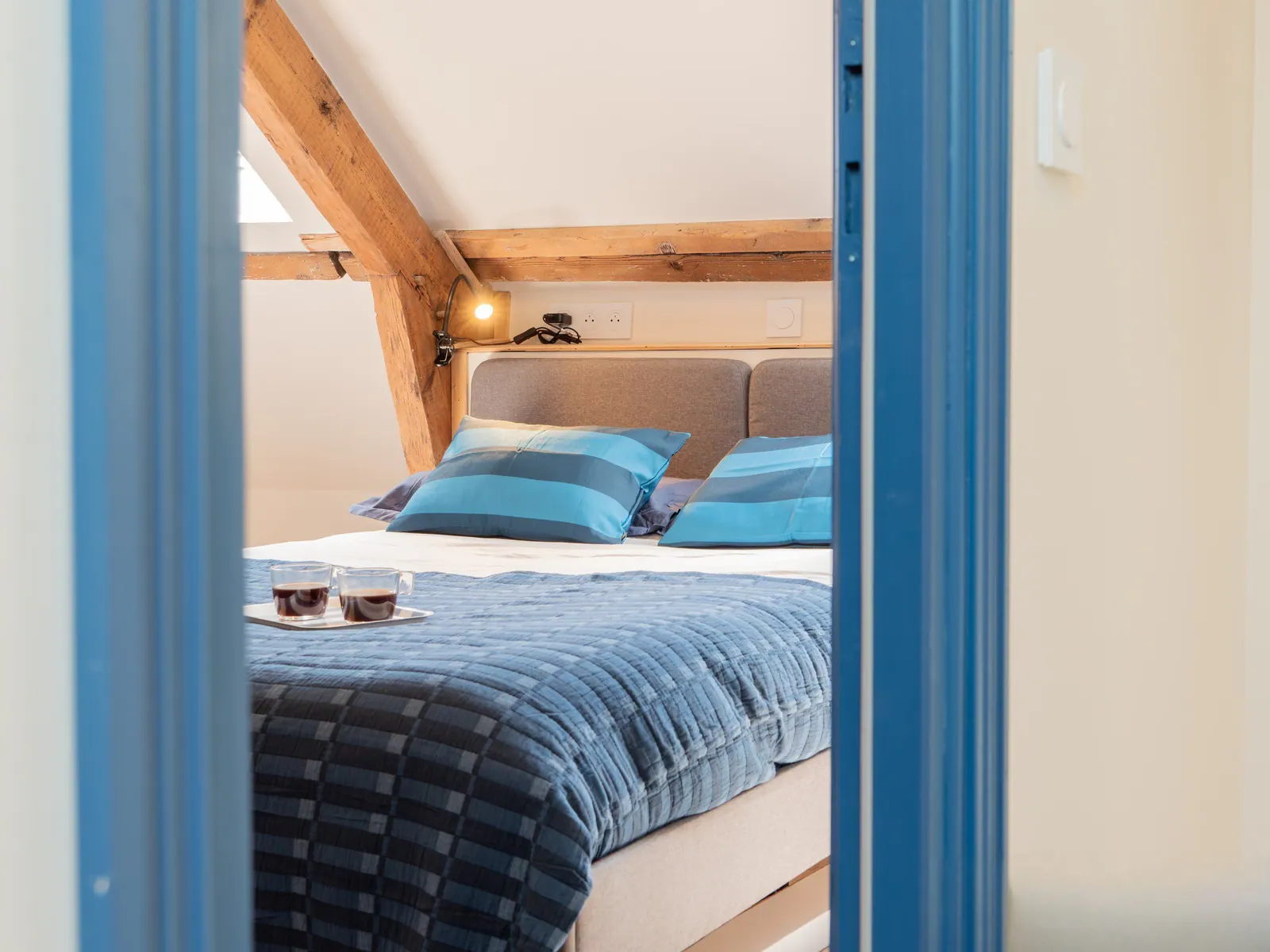 Chambre d'hôte aménagée avec poutres en bois, lit confortable et oreillers bleus