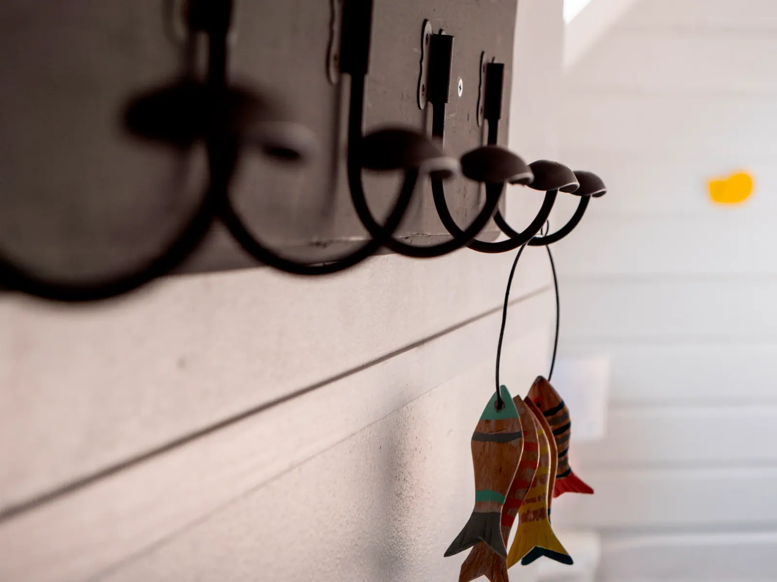 Rangée de crochets noirs avec poissons en bois peint suspendus sur mur blanc