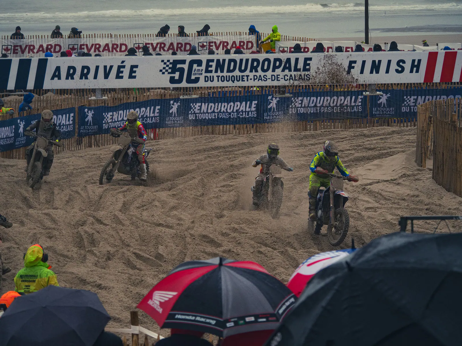 Motocyclistes en compétition sur le sable de la plage du Touquet lors de l'Enduropale, public et barrières visibles