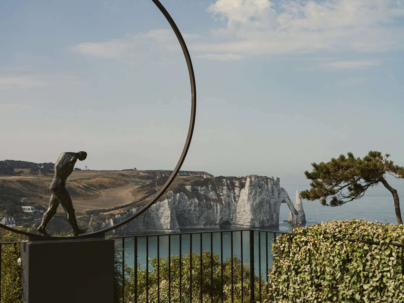 Sculpture de femme et falaises blanches d'Étretat face à la mer, vue depuis terrasse avec pin et haies