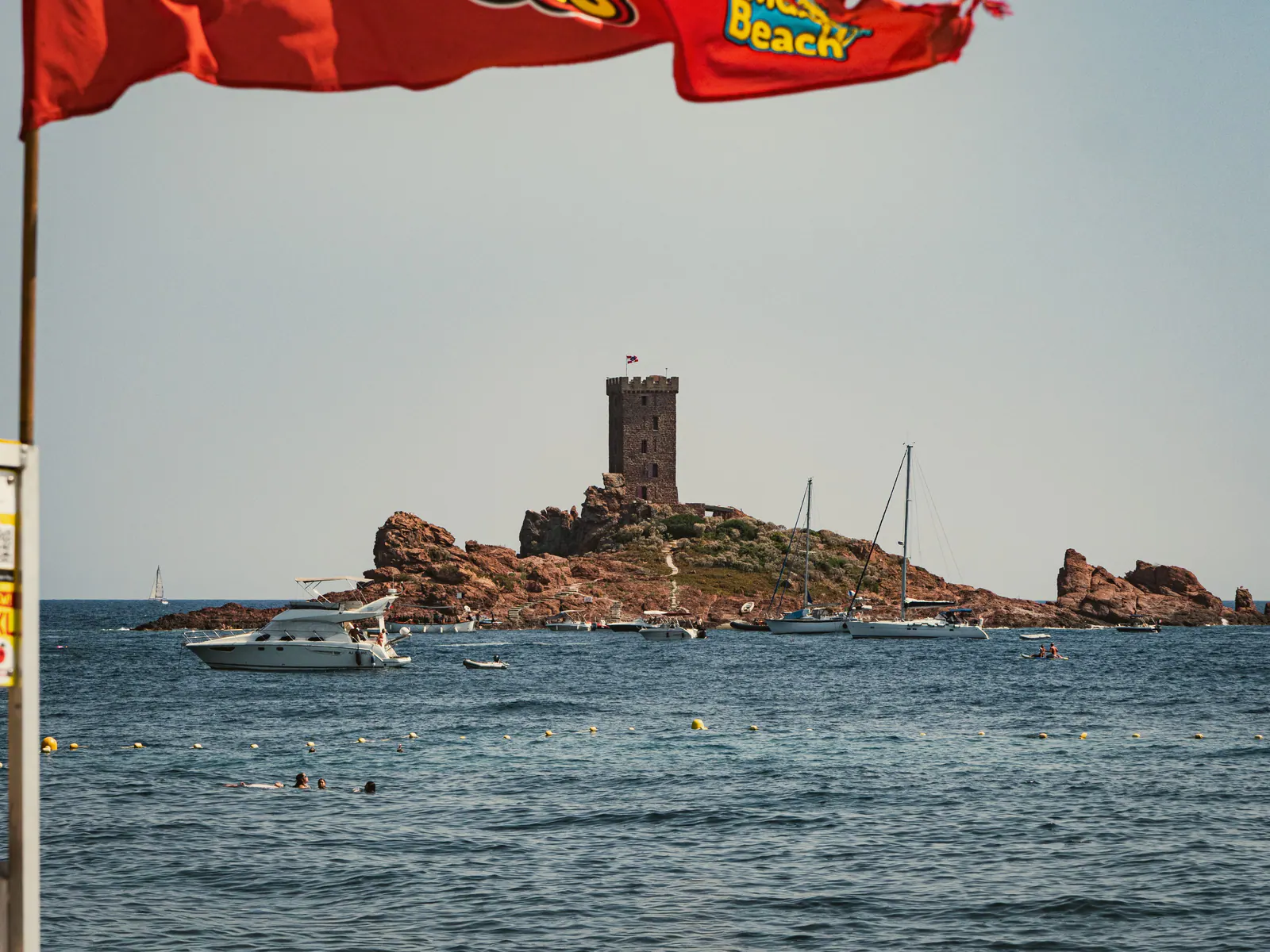 Vue sur l'ile du Dramont avec sa tour génoise, bateaux de plaisance et baigneurs en Côte d'Azur