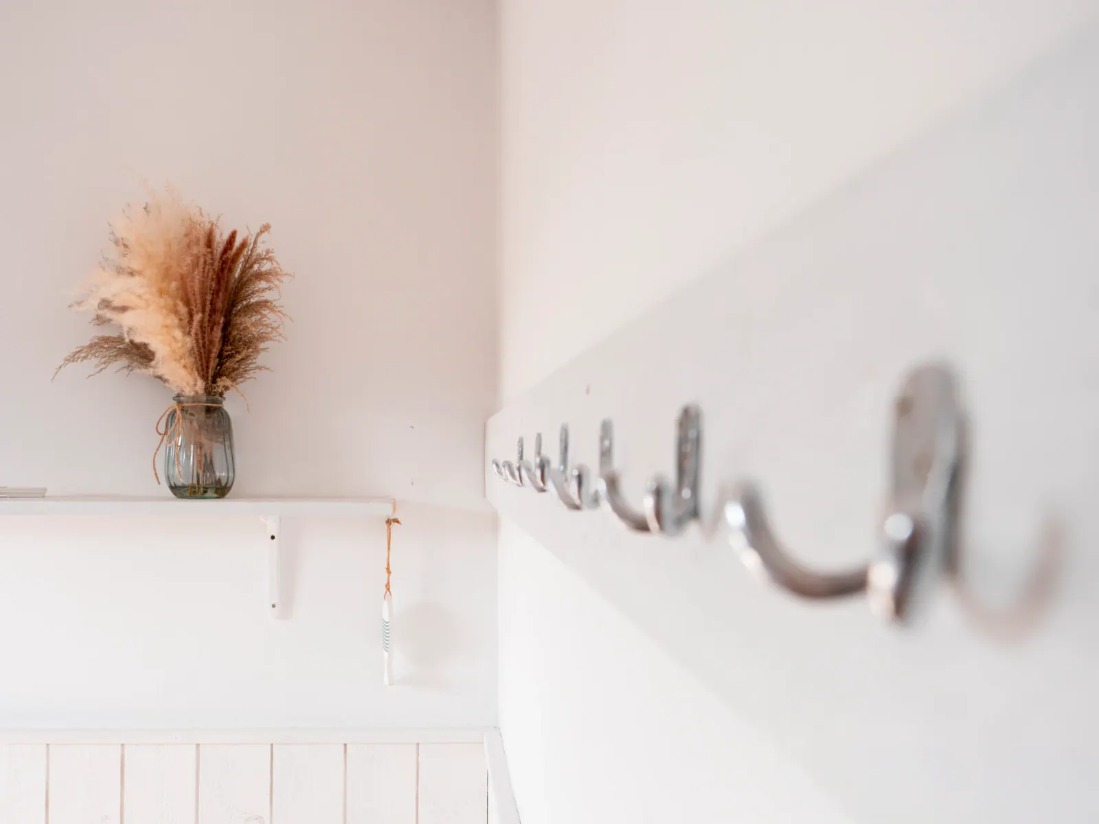 Intérieur minimaliste avec vase en verre et pampa dorée, crochet mural blanc sur mur blanc