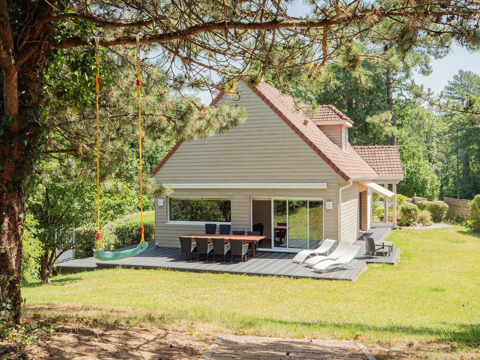 Maison contemporaine avec terrasse en bois, salon de jardin et balançoire sous les arbres
