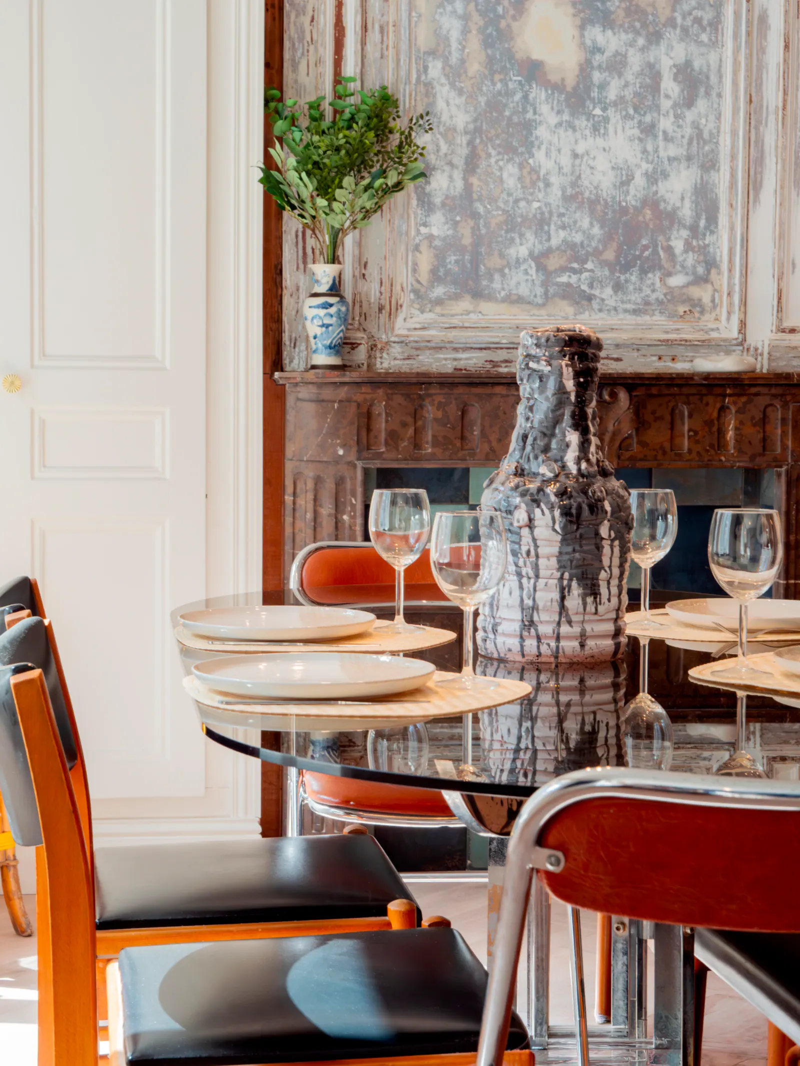 Salle à manger contemporaine, table ronde en bois, chaises orange, cheminée pierre, miroir ancien