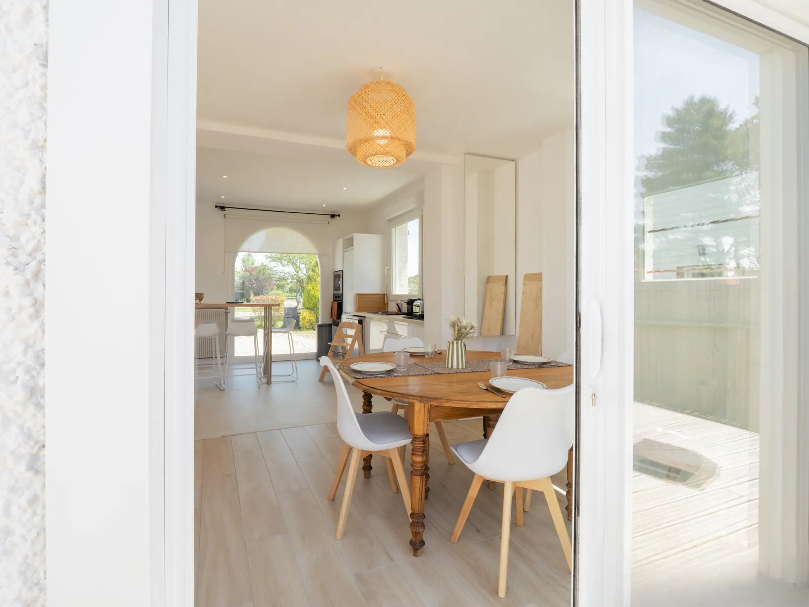 Salle à manger moderne avec table en bois, chaises blanches et baies vitrées ouvertes sur terrasse et jardin