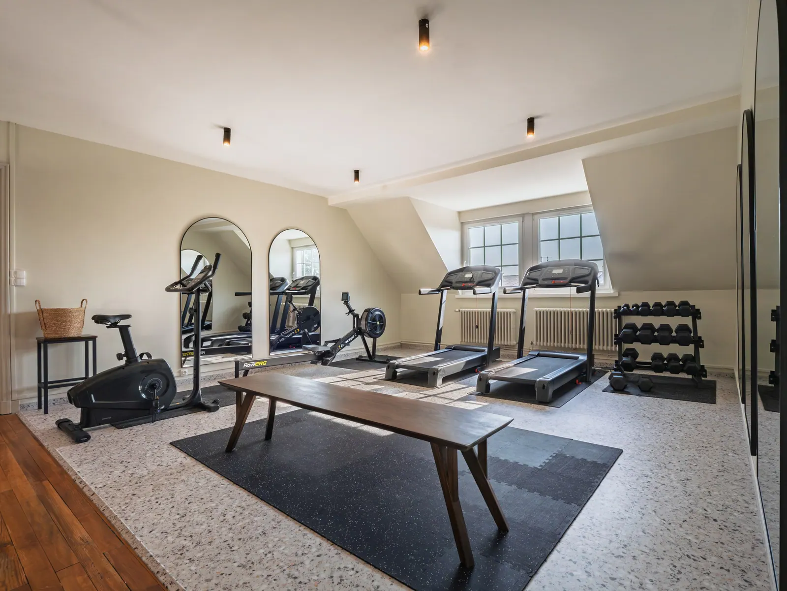 Salle de sport privée moderne avec tapis de course, vélos et miroirs muraux, luminaire design, baies vitrées