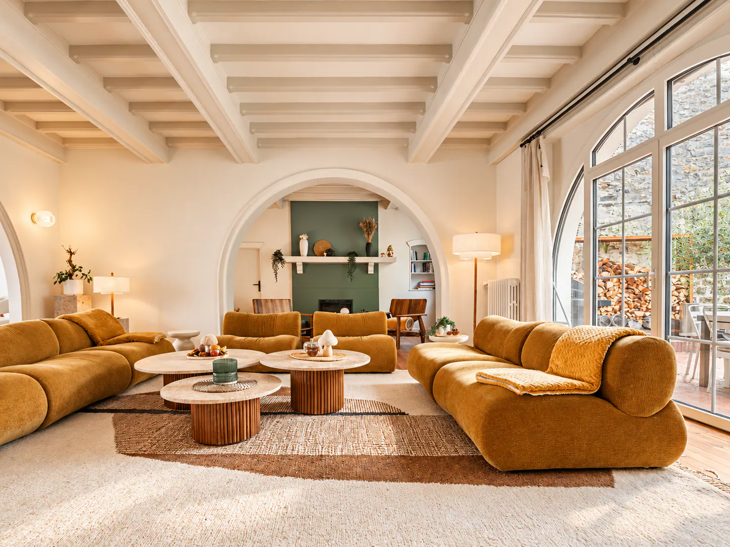 Vaste salon contemporain avec canapés ocre arrondis, poutres apparentes blanchies, alcôve verte et grandes baies vitrées sur la côte