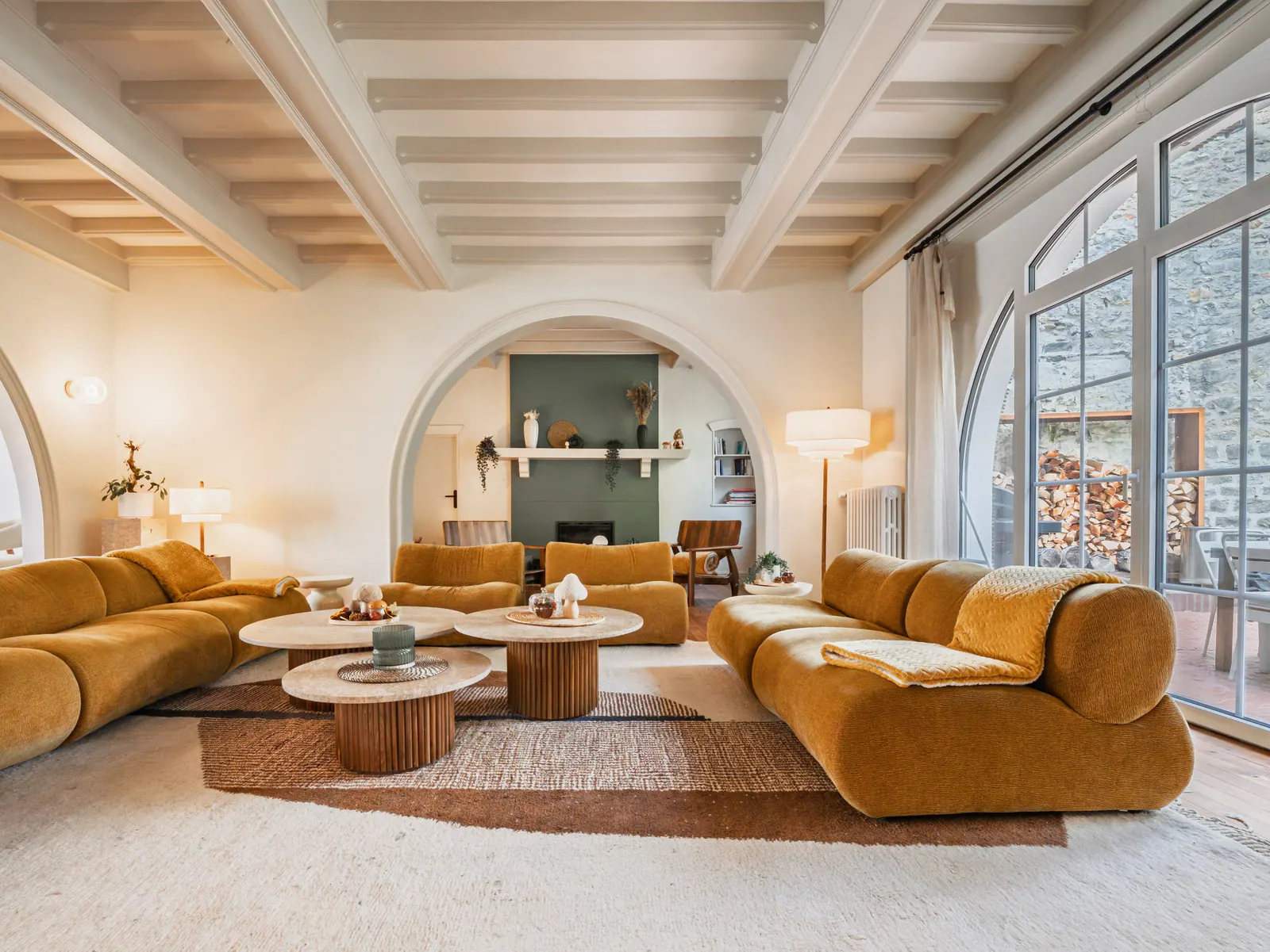 Vaste salon contemporain avec canapés ocre arrondis, poutres apparentes blanchies, alcôve verte et grandes baies vitrées sur la côte