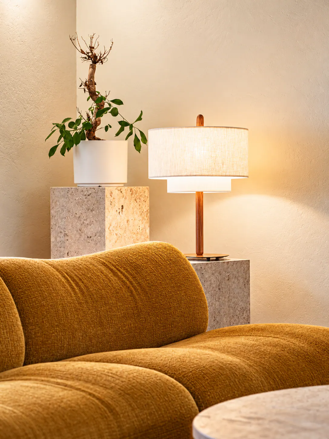 Salon élégant avec canapé ocre, lampadaire bois, plantes et mobilier gris béton