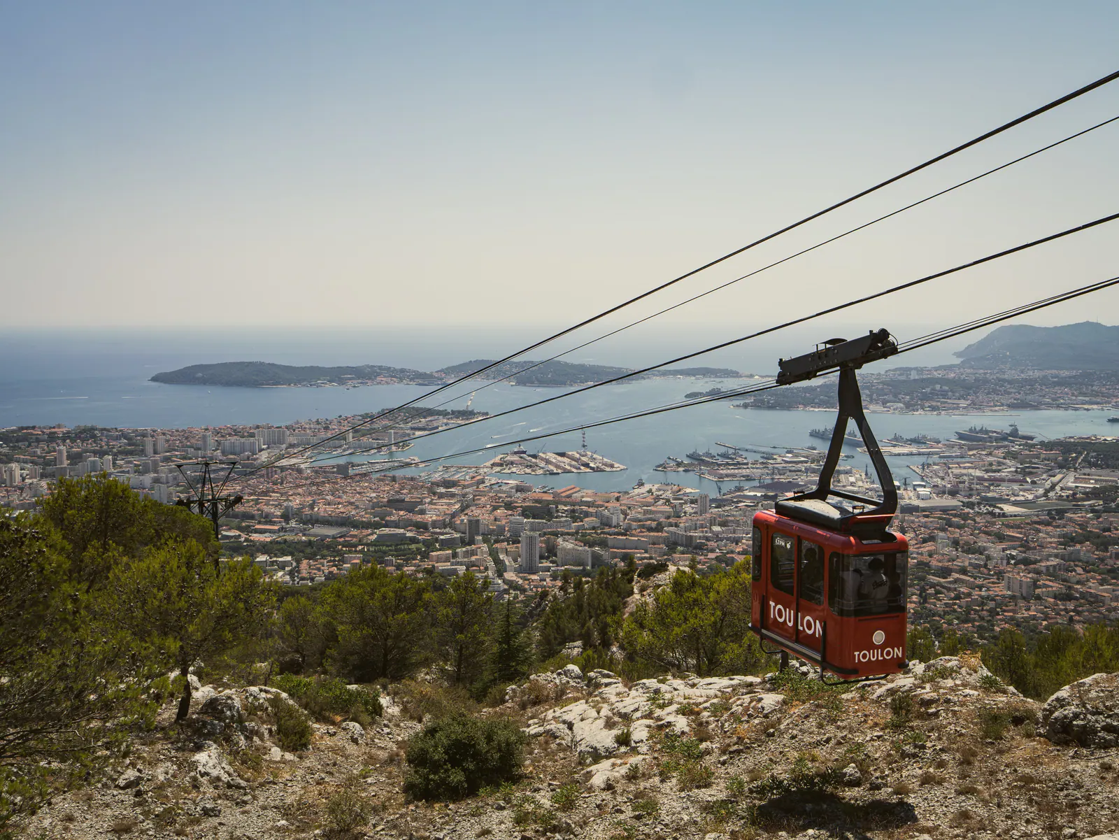 Téléphérique rouge surplombant la baie de Toulon avec vue panoramique sur la côte méditerranéenne