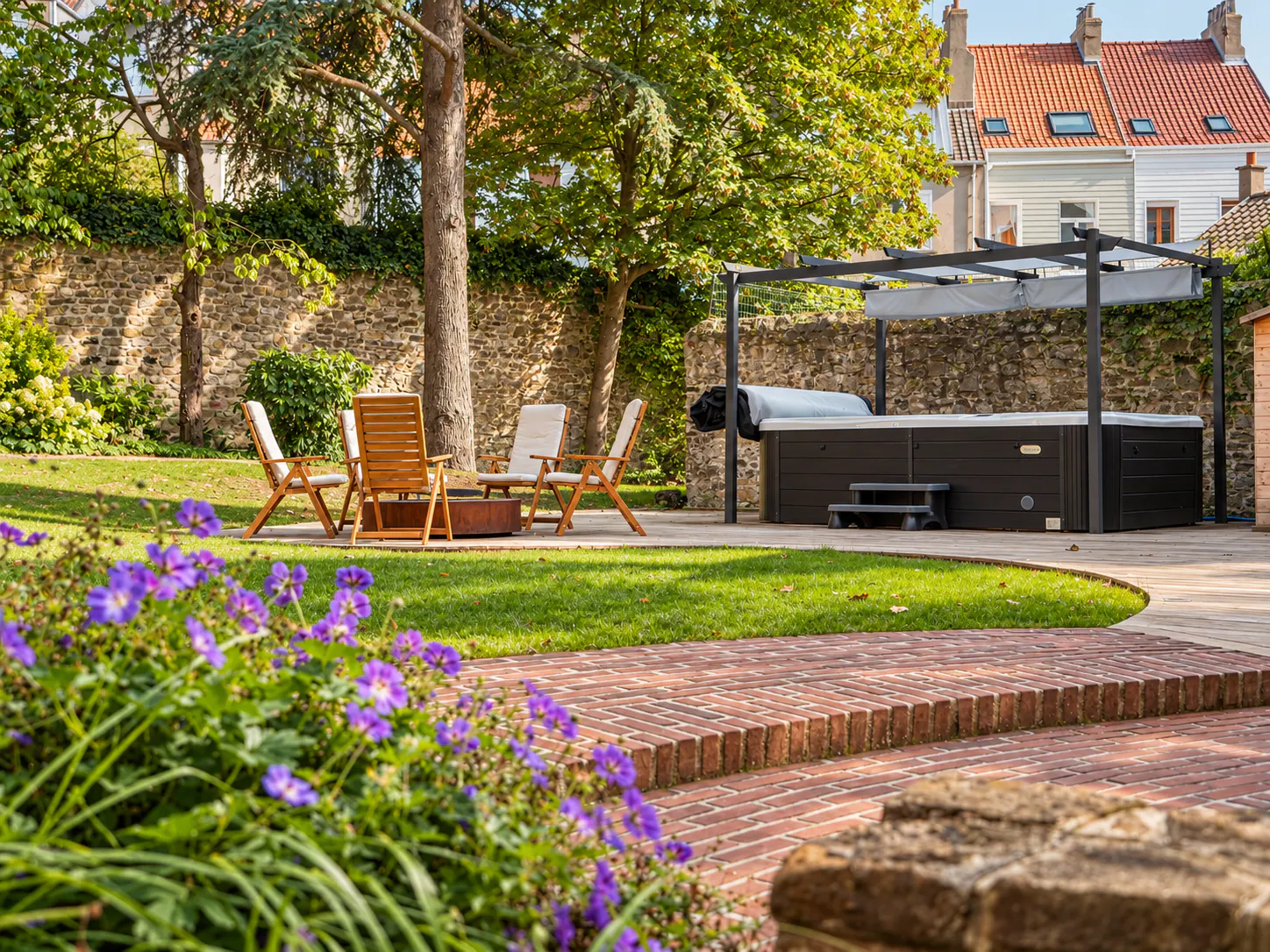 Jardin et terrasse aménagée avec jacuzzi sous pergola, chaises longues et fleurs violettes