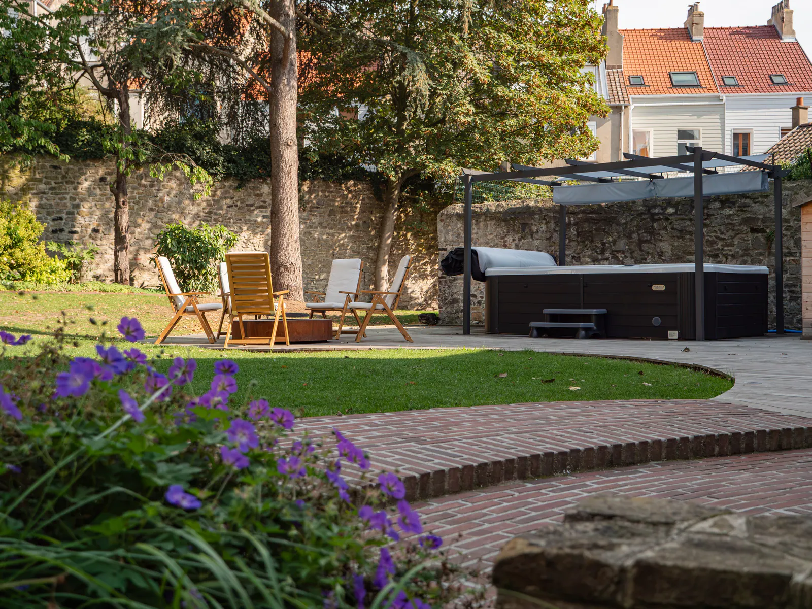 Jardin et terrasse aménagée avec jacuzzi sous pergola, chaises longues et fleurs violettes