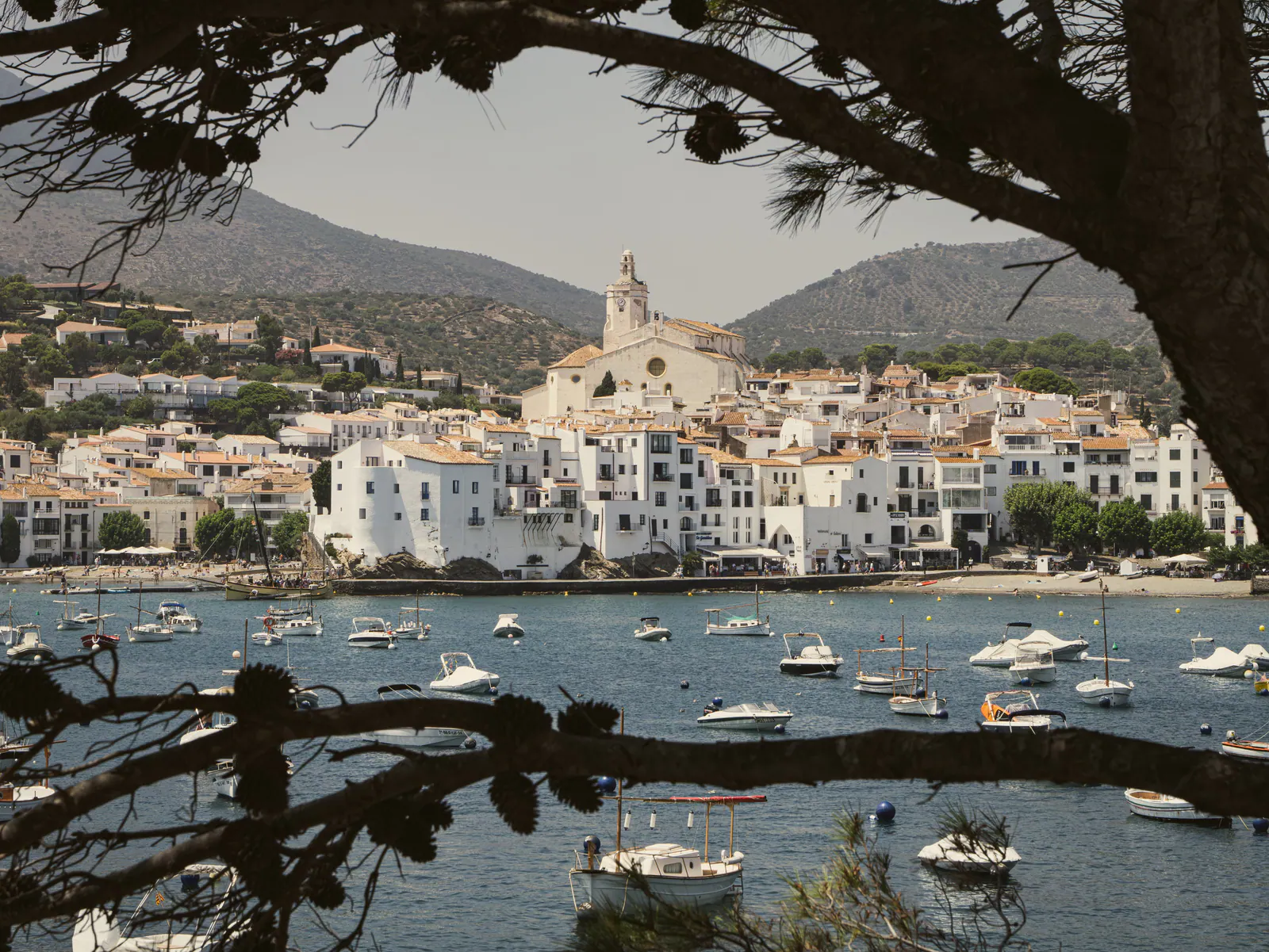Vue panoramique d'un village côtier méditerranéen avec église blanche, maisons traditionnelles et bateaux amarrés
